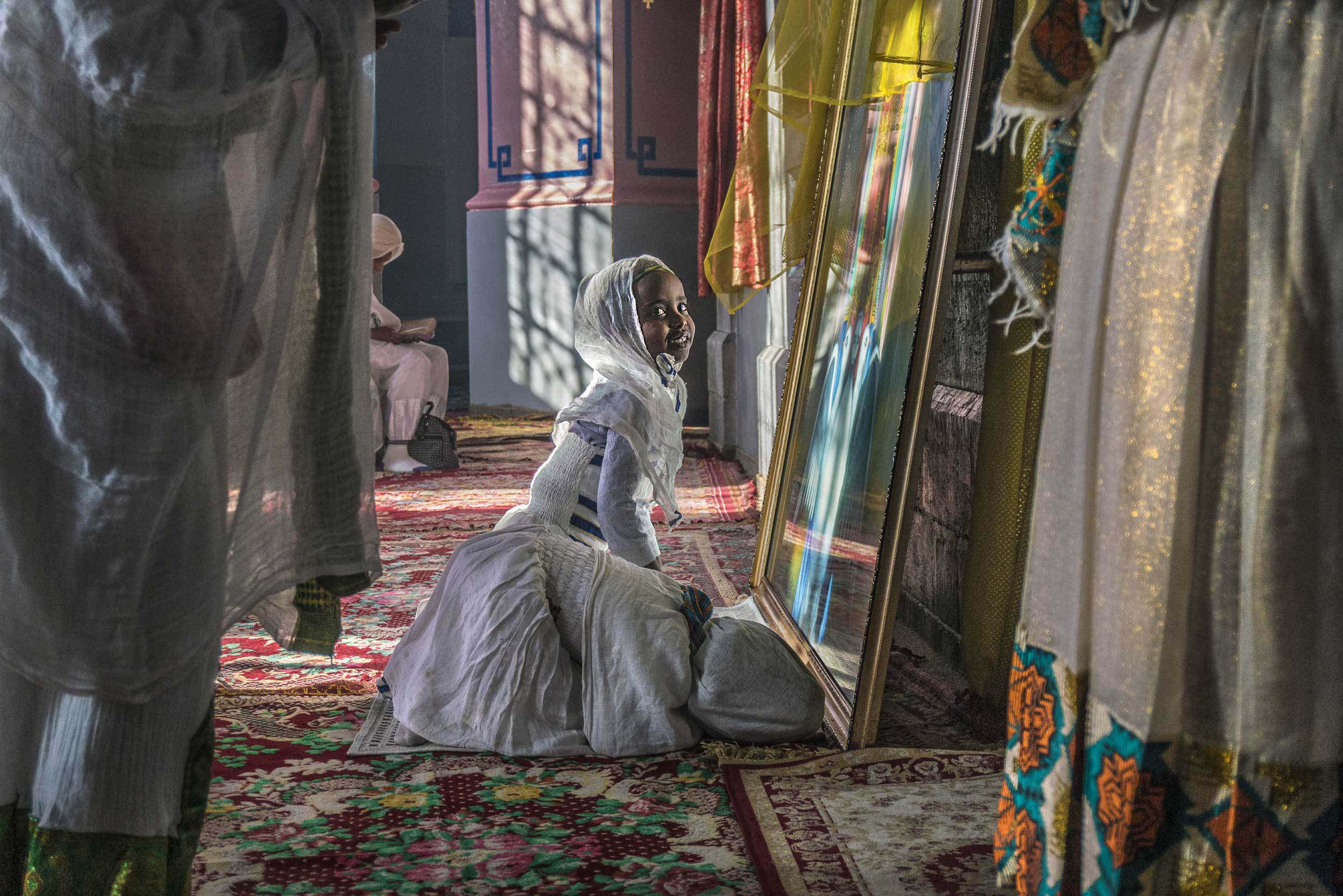 A kneeling girl in front of a mirror dressed in white and a head scarf, Jerusalem