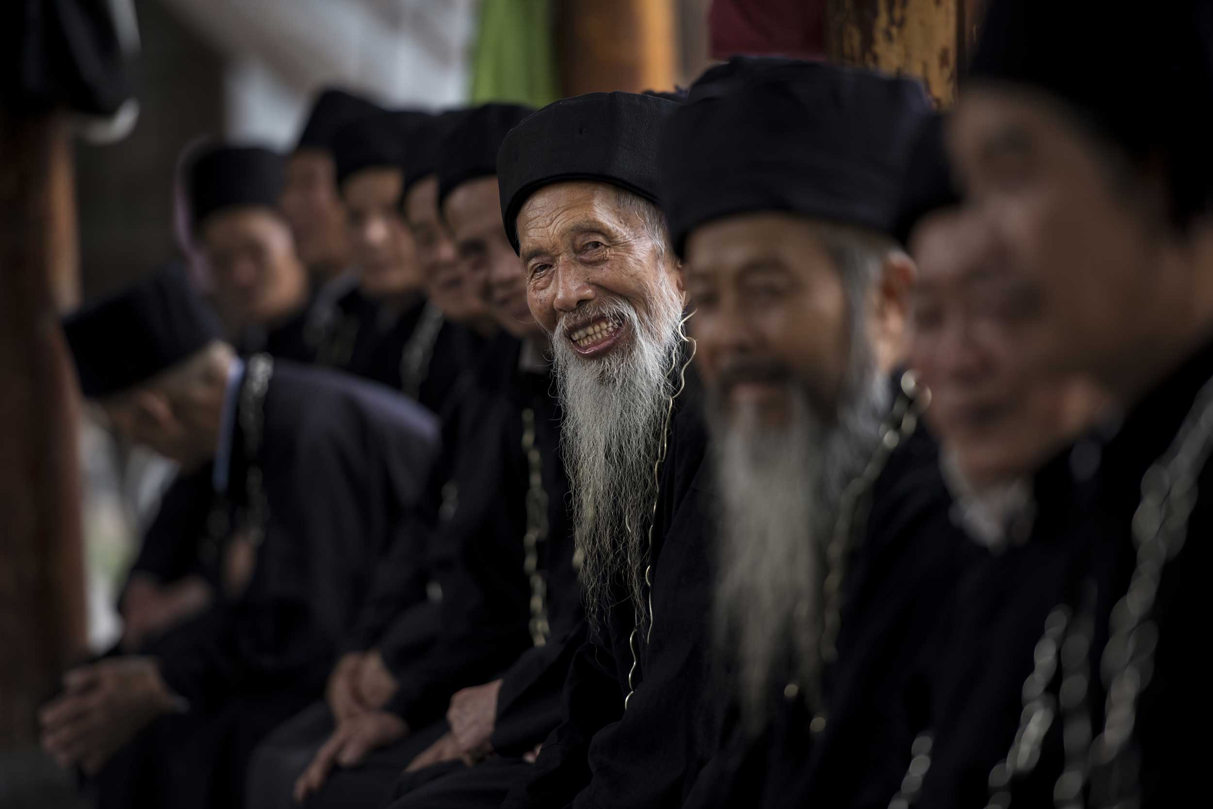 An old bearded Chinese man amongst other faces looking at camera, China