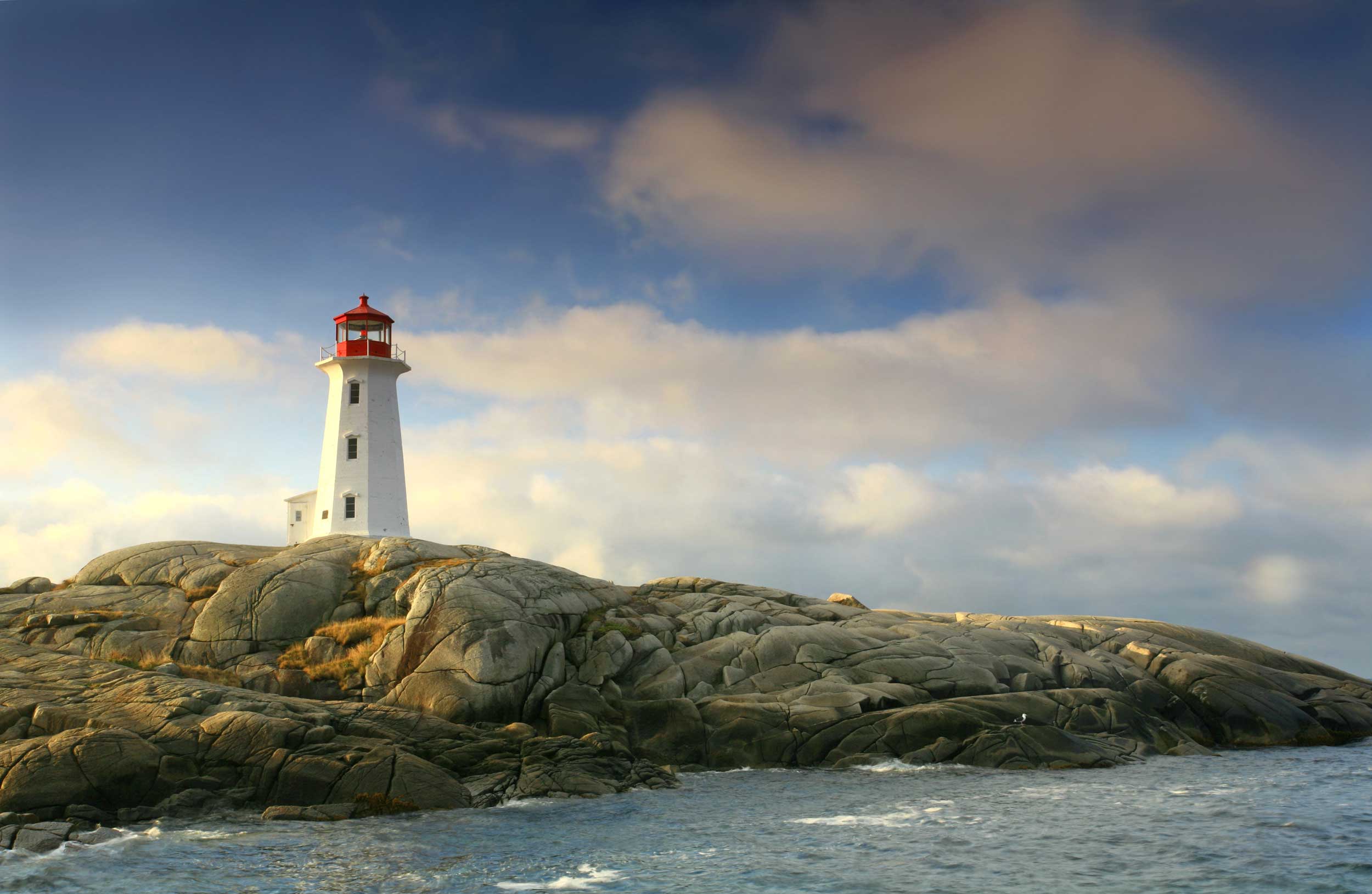 A white lighthouse with a red top set on a smooth-rock promontory, Peggy's Cove, Halifax