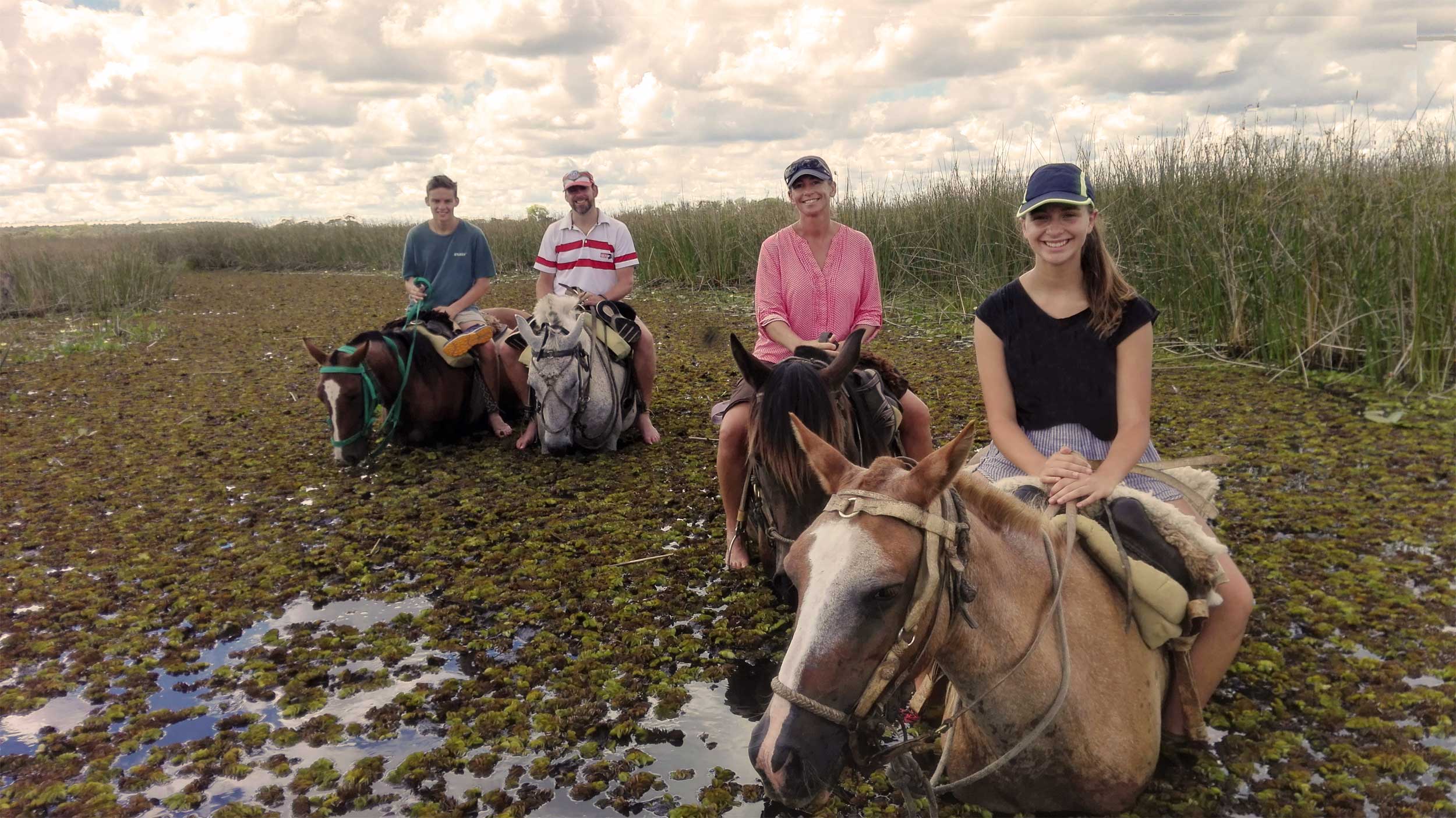 Family of four on horseback in water hyacinth-strewn waterway, Argentina