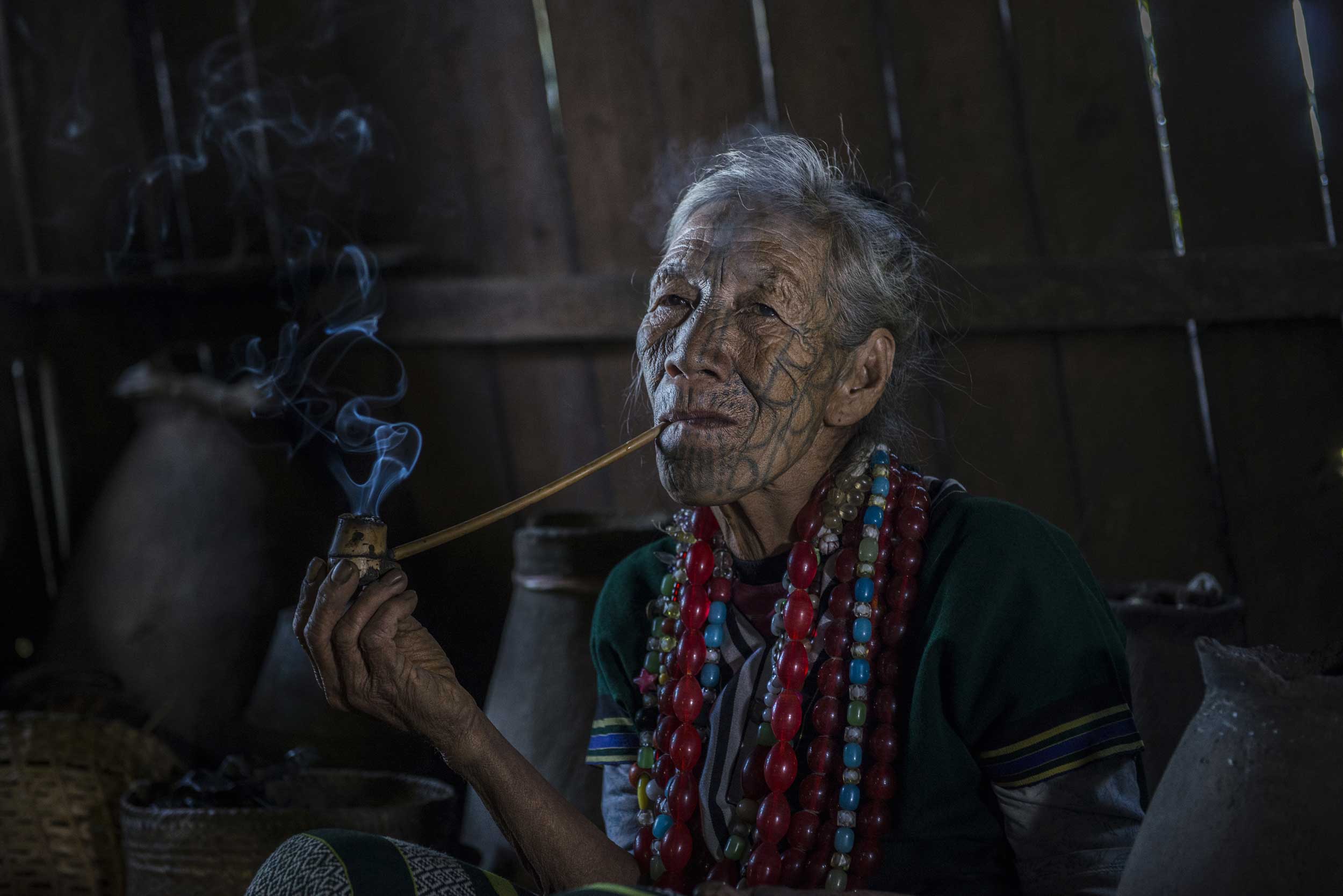 Elderly woman with a tattooed face smoking a pipe, Myanmar