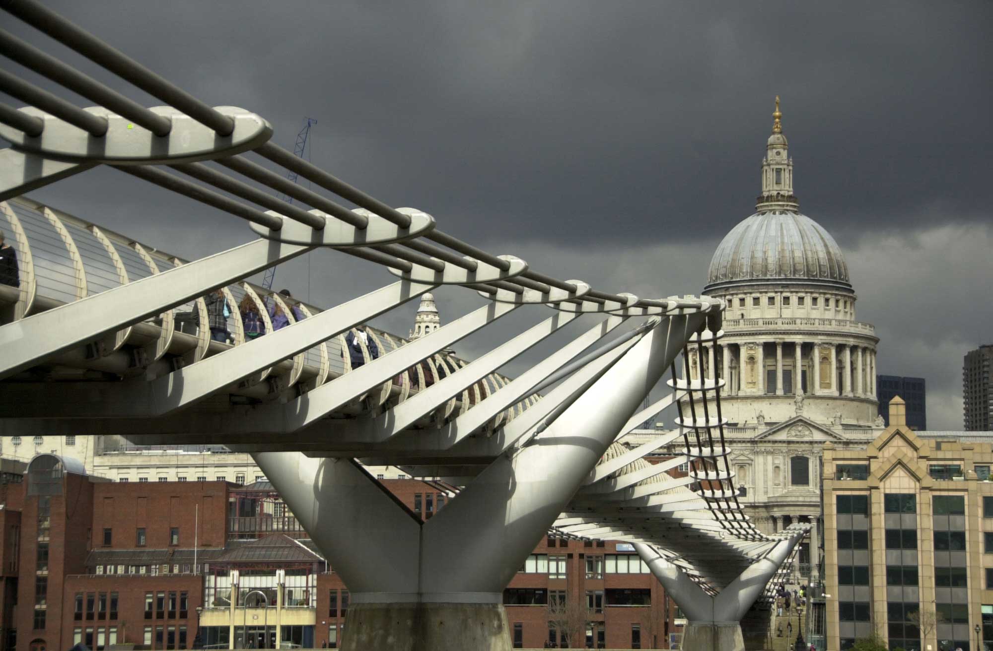 An undulating suspension bridge leading towards an ancient domed cathedral, London