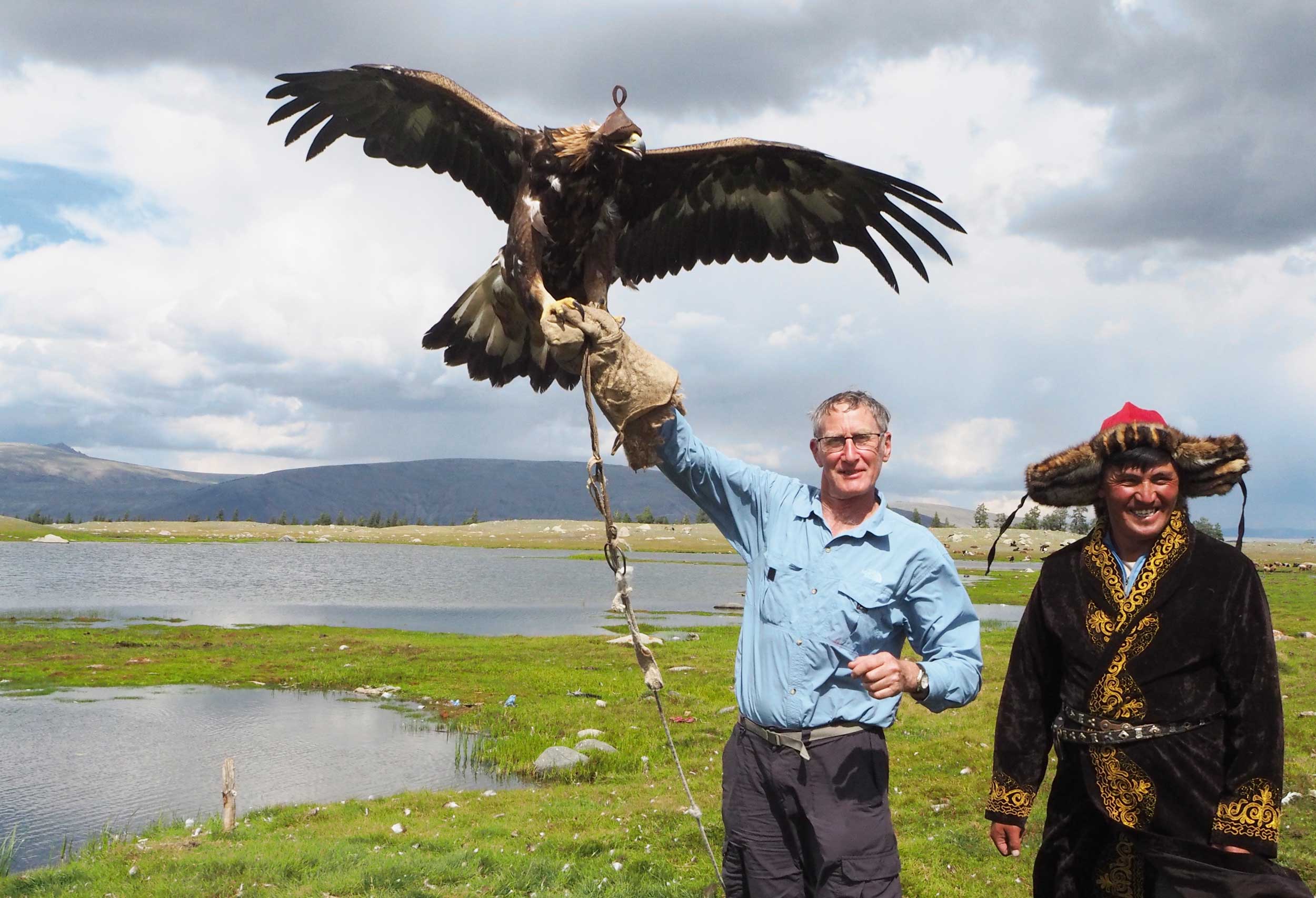 A western man holding an eagle aloft with a smiling Mongolian man next to him.