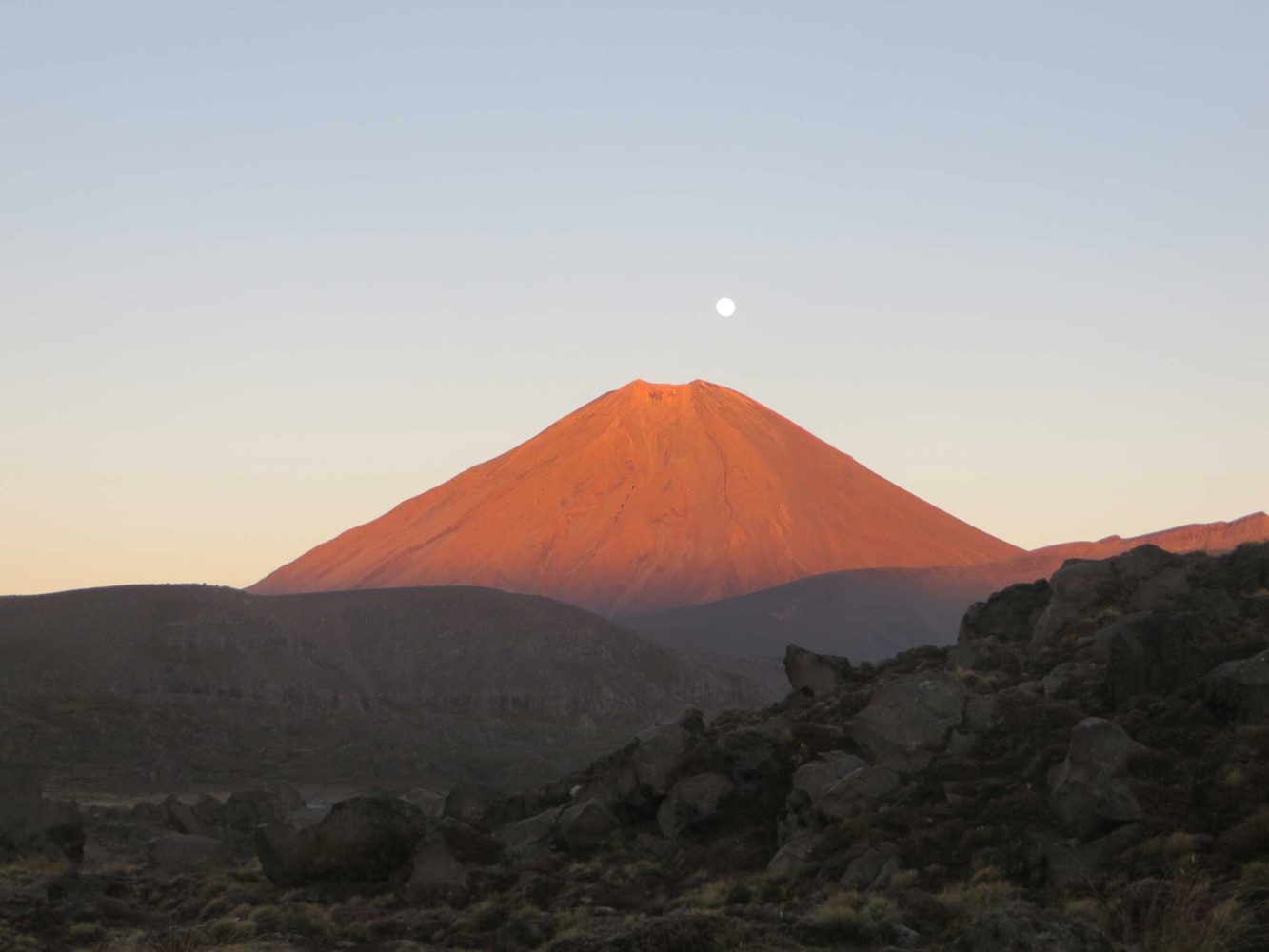 Moon setting behind a red Mt Ngauruhoe at sunrise, New Zealand